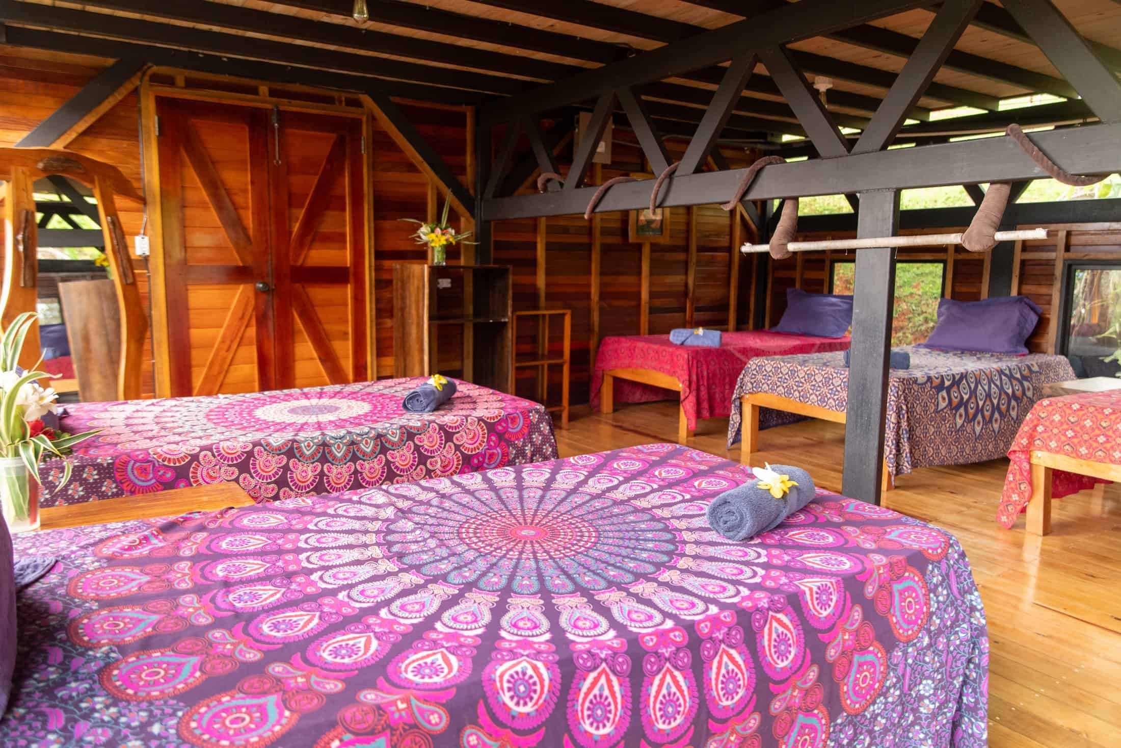 Aerial studio guest dorm with hand-built timber trusses and beds dressed in bright mandala tapestries at Airborne Arts