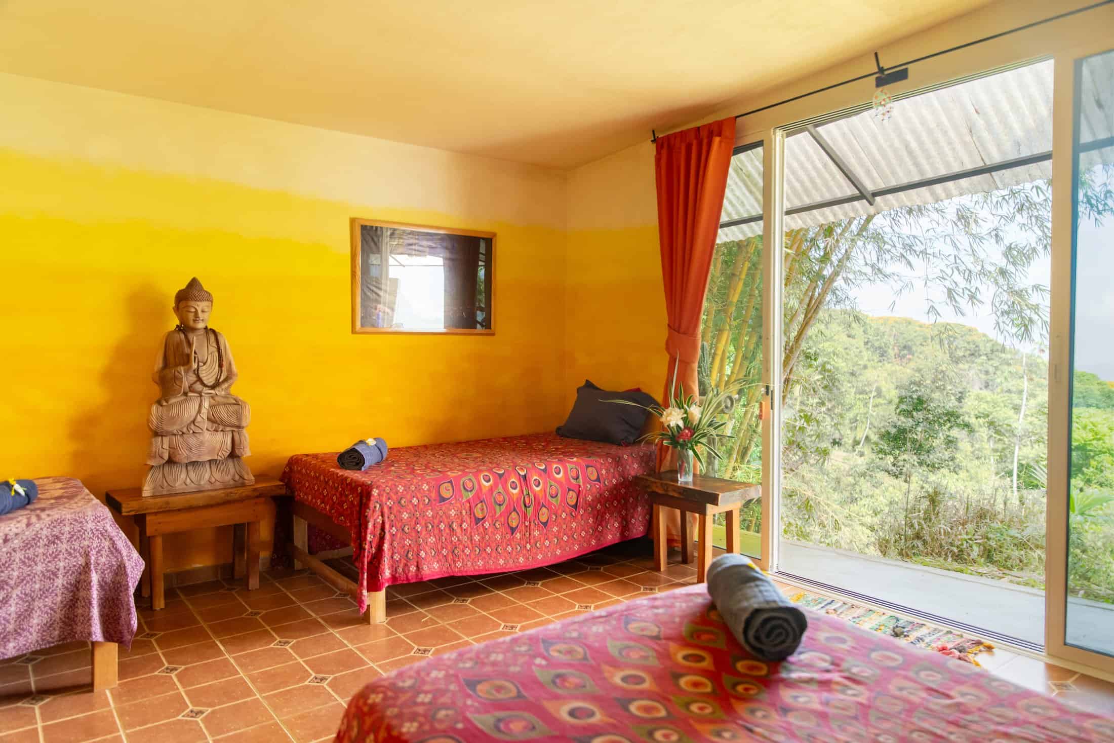 Avalon Guest Room with sun-warmed yellow walls, hand-carved Buddha statue and sliding glass doors onto the jungle