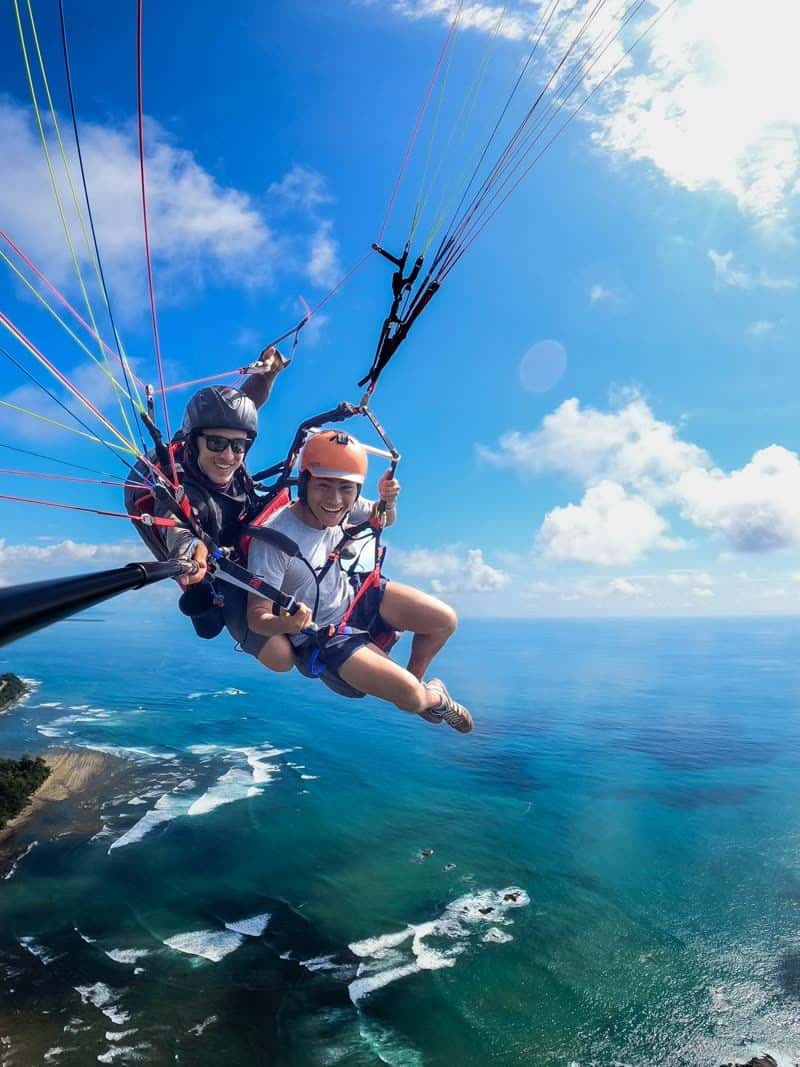 Tandem paragliding over the Pacific coast and jungle canopy near Dominical, Costa Rica with mountain ridgelines below