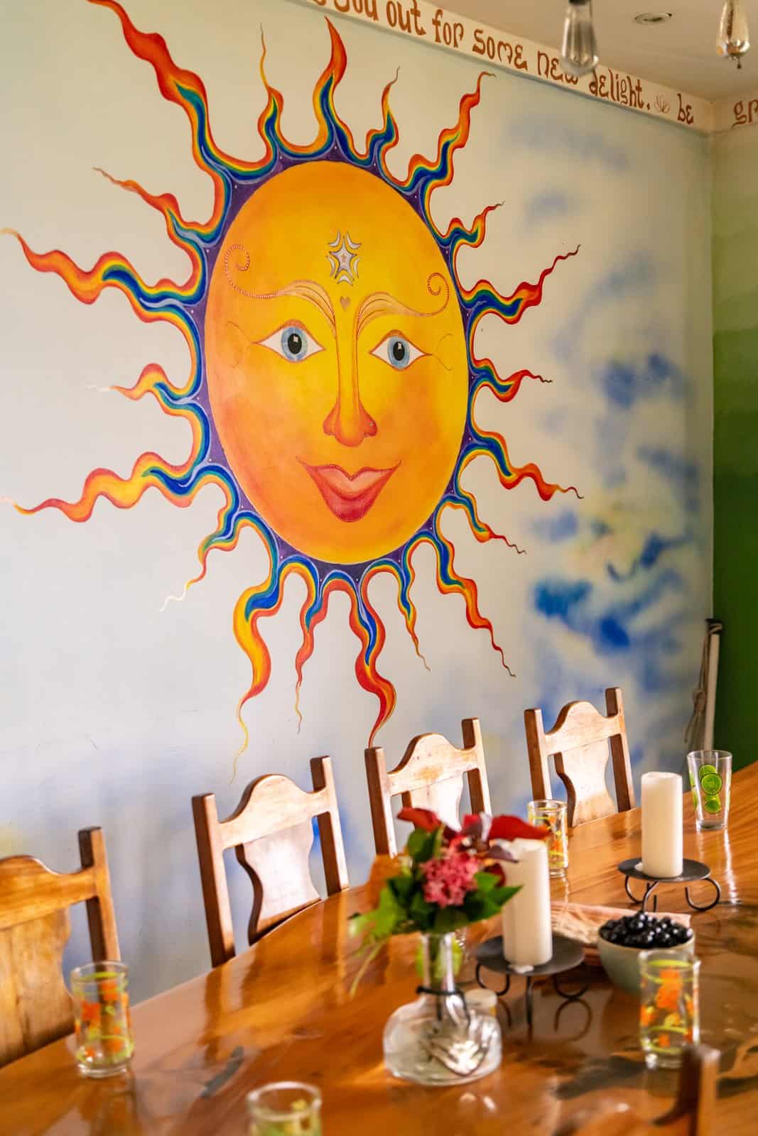 The communal dining table beneath a hand-painted sun mural at Airborne Arts