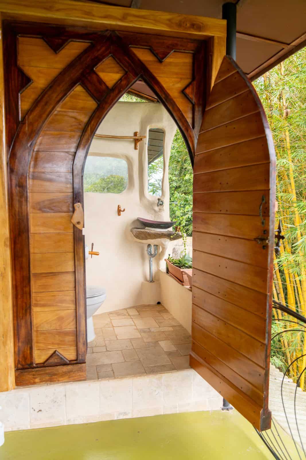 Gothic-arched wooden door opening to the Master Suite bathroom with bamboo and jungle outside